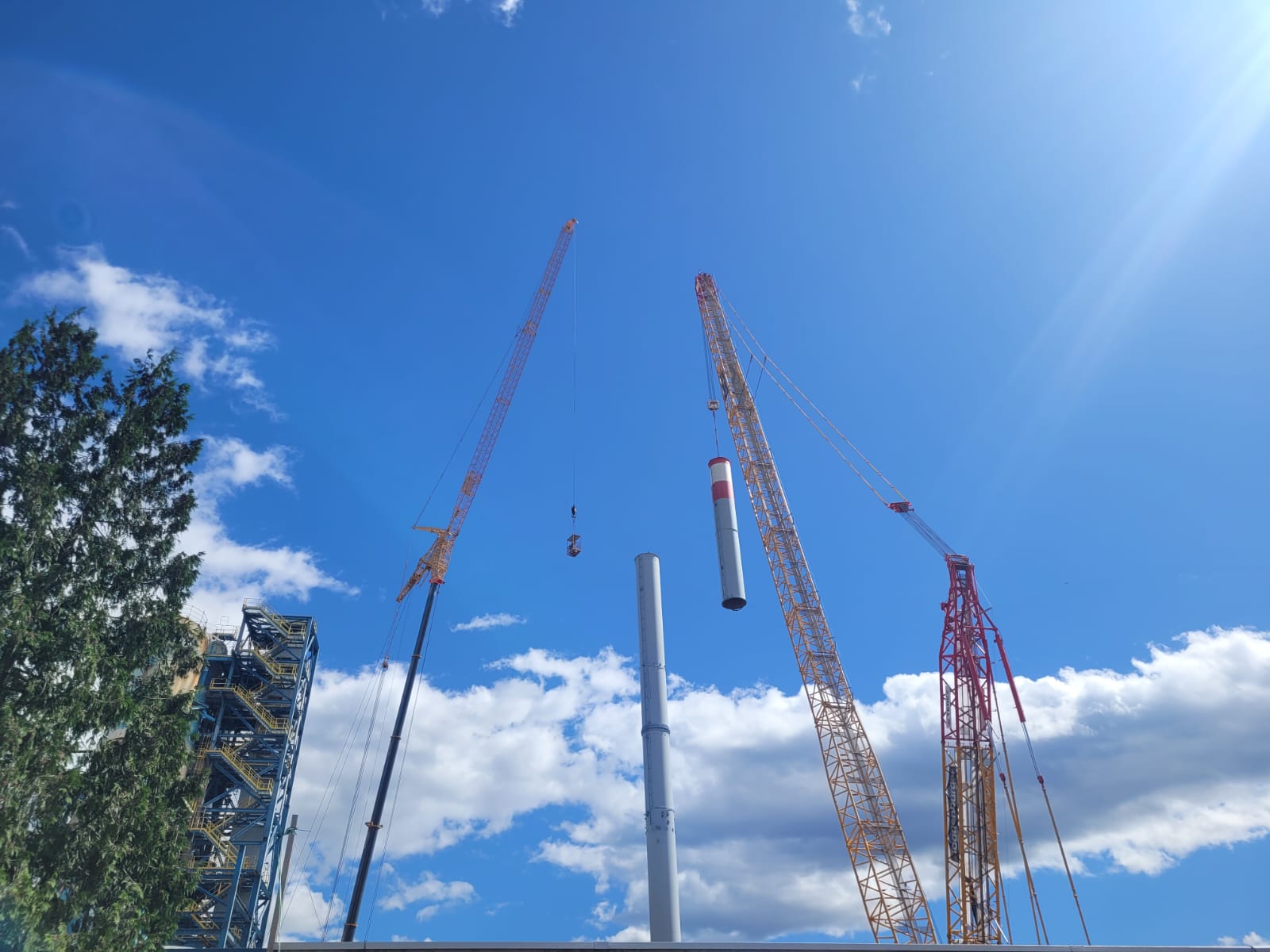 Cranes lifting a chimney section against a blue sky